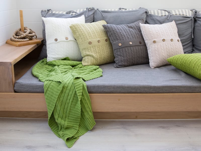 Green throw on a grey couch with knitted cushions.