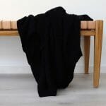 An image of a black knitted throw blanket draped over a stool