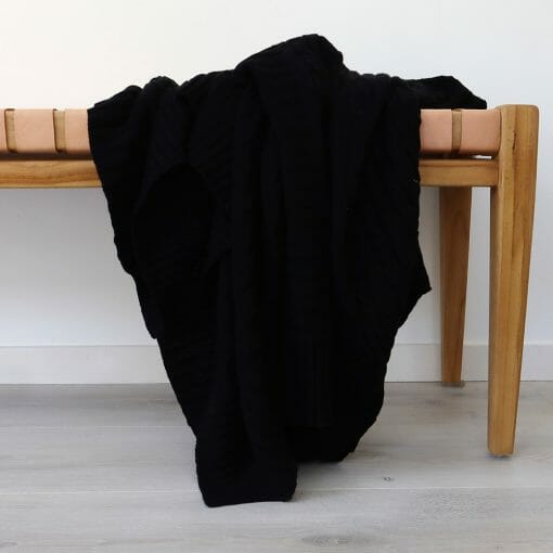 An image of a black knitted throw blanket draped over a stool