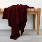 An image of a burgundy knitted throw blanket draped over a stool