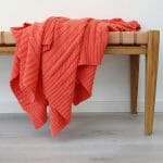 An image of a coral knitted throw blanket draped over a stool