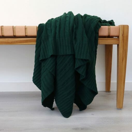 An image of a emerald green knitted throw blanket draped over a stool