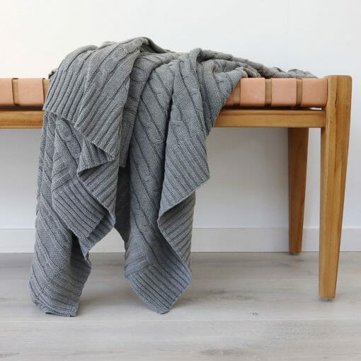 An image of a grey knitted throw blanket draped over a stool