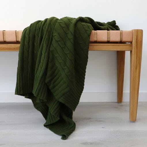 An image of a olive green knitted throw blanket draped over a stool