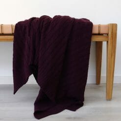 An image of a purple knitted throw blanket draped over a stool