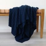 An image of a royal knitted throw blanket draped over a stool