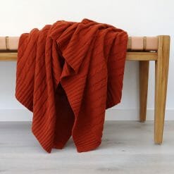 An image of a rust coloured knitted throw blanket draped over a stool