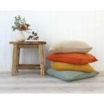 Stack of neutral cushions in terracotta, mustard and sage abasing a white wall