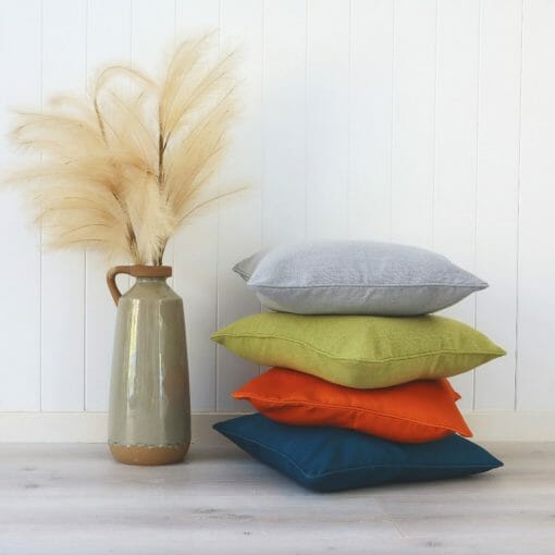 Stack of bright coloured cushions next to a vase with ferns against a wall