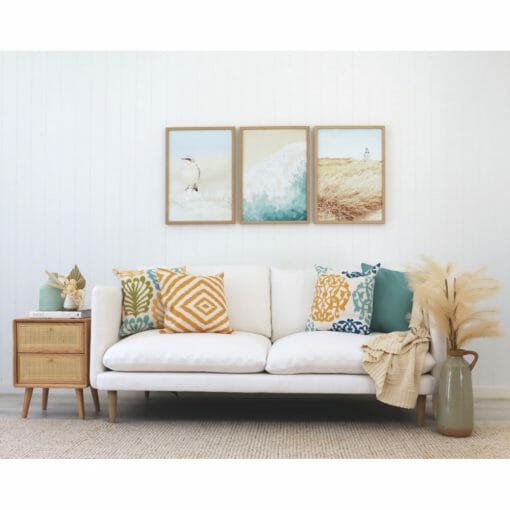 Coastal cushions in gold and teal on a white sofa with coastal wall art