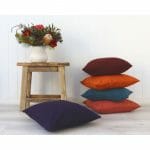 A stack of Burgundy, burnt orange and blue cushions against a white wall