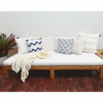 Beige throw and outdoor cushions in stripe, diamond, chevron and floral patterns on top of white wooden daybed.