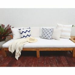 Beige throw and outdoor cushions in stripe, diamond, chevron and floral patterns on top of white wooden daybed.