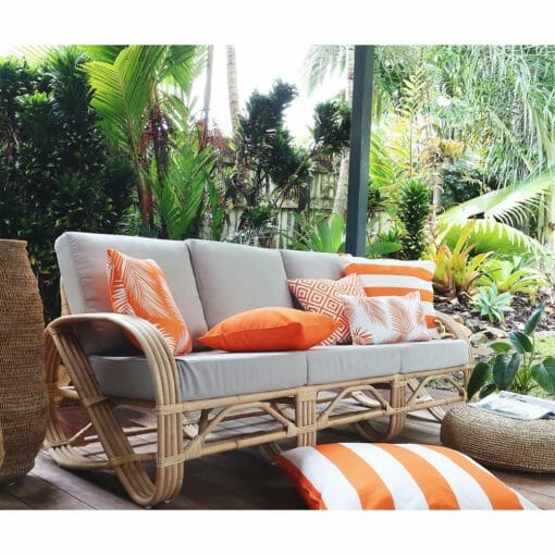 Bright orange outdoor cushions in stripe, diamond and floral patterns on top of grey rattan sofa