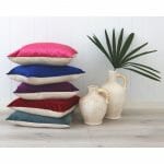 A stack of bright velvet linen cushions next to a vase
