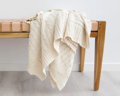 A beige throw blanket is draped over a wooden bench seat that features leather straps.