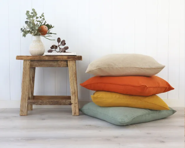 Four cushion covers are shown stacked next to a small wooden table.