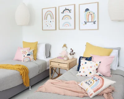 Kids cushion covers in pink, blue and yellow styled on two beds in a children’s bedroom.