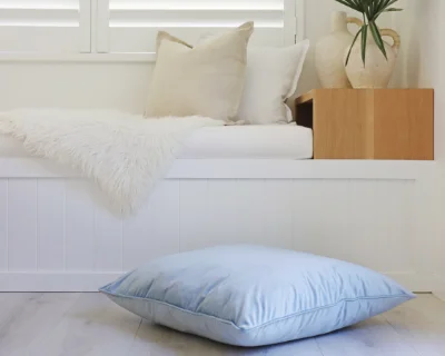A large floor cushion in light blue sits in front of a white window seat.