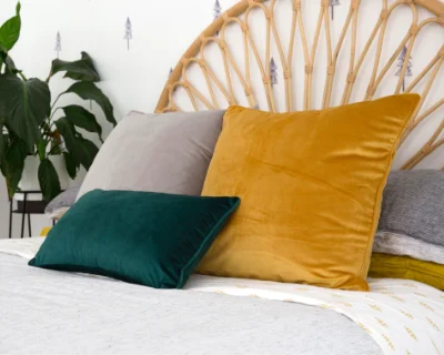 A bed decorated with three velvet cushions in grey, green and mustard.