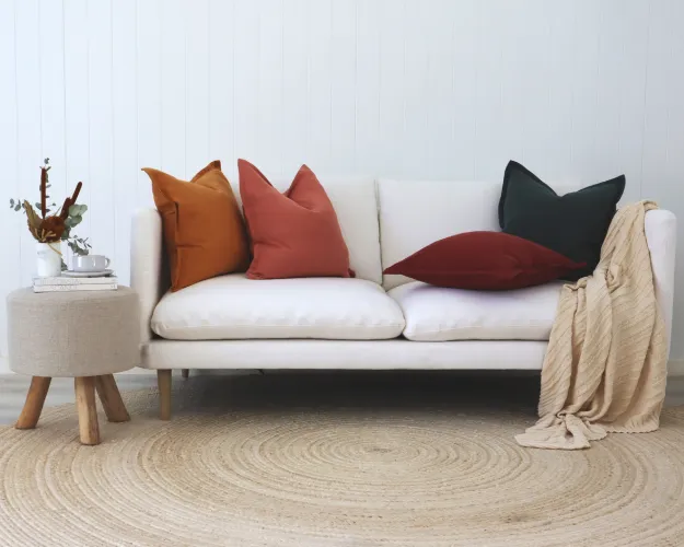 A white living room with four colourful linen cushions styled on a couch.