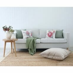 White living room with wooden table, woven carpet, luxurious velvet floor cushion, sage green throw and cushions in sage green and floral prints