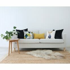 Neutral-coloured sofa with wooden side table, light brown rug and gold and navy cushions with geometric prints