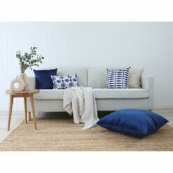 Light-coloured sofa with wooden side table, woven rug, navy cushions with shibori prints