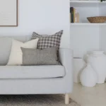 A light grey sofa in a living room that has white walls styled with 5 designer sofa cushions.