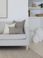 A light grey sofa in a living room that has white walls styled with 5 designer sofa cushions.