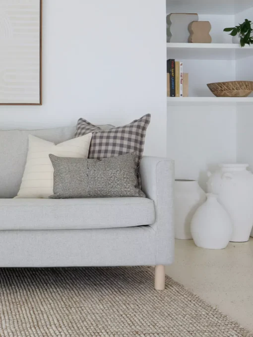 A light grey sofa in a living room that has white walls styled with 5 designer sofa cushions.