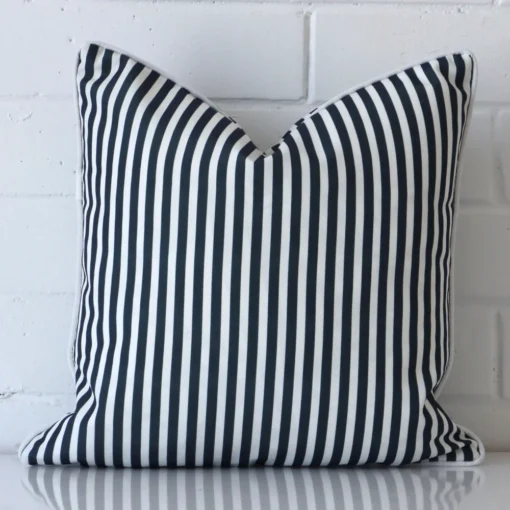 Bold square blue cushion positioned in front of white brickwork. Its striped style pops on the outdoor fabric.