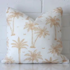 An attractive palm tree outdoor cushion in front of a white brick wall. It has a square shape and is beige in colour.