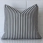 Black and white striped cushion cover sits against a white wall. It is constructed from a superior looking outdoor material and has square dimensions.
