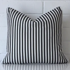 Black and white striped cushion cover sits against a white wall. It is constructed from a superior looking outdoor material and has square dimensions.