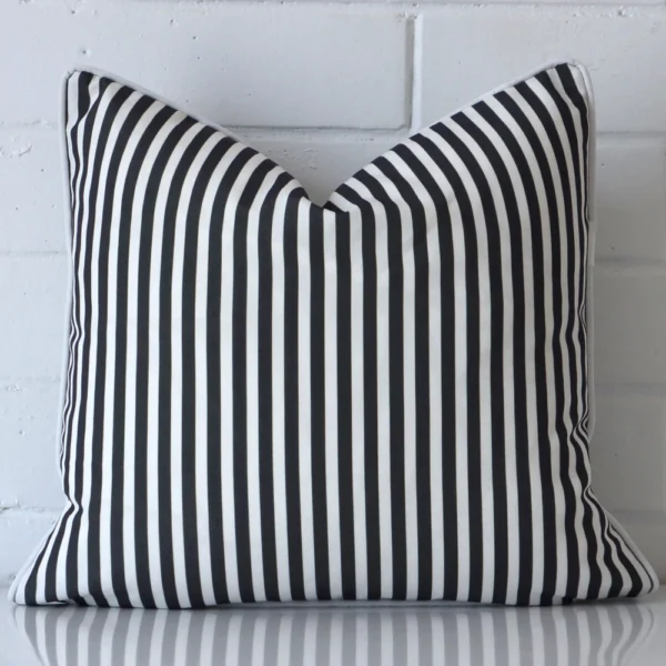 Black and white striped cushion cover sits against a white wall. It is constructed from a superior looking outdoor material and has square dimensions.