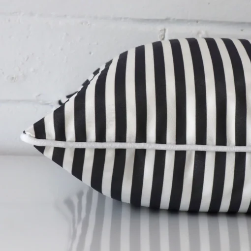 A sideways perspective of this striped outdoor cushion. The positioning shows the border of the square shape and the black and white colour.