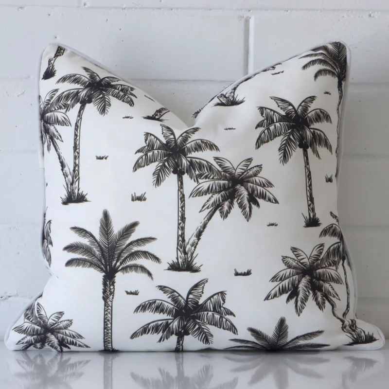 Airlie Palm Tree Waterproof Black and White Outdoor Cushion Cover - SC905-45 White wall with a palm tree black and white cushion laying against it. It has a distinctive outdoor fabric and has a square shape.