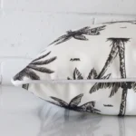Square palm tree cushion cover in black and white colour sitting flat. The sideways viewpoint shows the seams of the outdoor material.