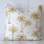 Square palm tree cushion cover in mustard colour sitting upright in front of a brick wall. It has been made from a quality outdoor material.