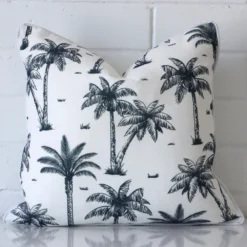 Outdoor square cushion with a palm tree design in an upright position against a white brick wall. It is navy blue in colour.