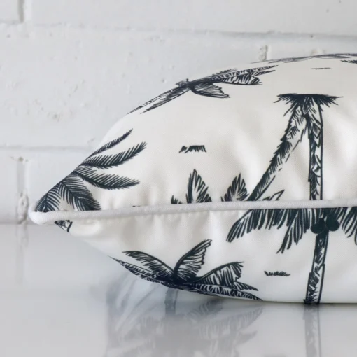 Square navy blue cushion laid flat. This view shows the palm tree style and outdoor fabric from side on.