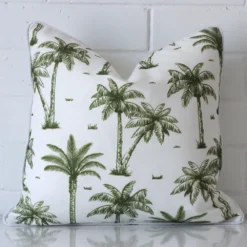 Olive green outdoor cushion cover features prominently against a white wall. It is a square design and has a palm tree decorative finish.
