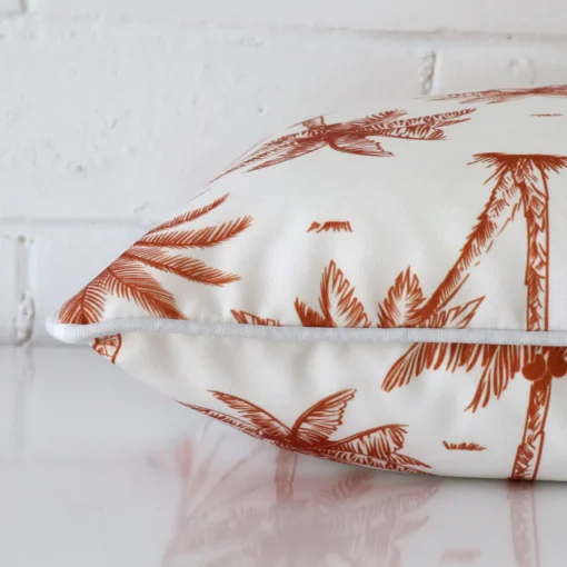 Palm tree terracotta cushion laid horizontally. This perspective shows the edge of the outdoor fabric and its square shape.