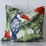 Toucan tropical cushion cover in front of a white wall. It has a square size and is made from a outdoor material.