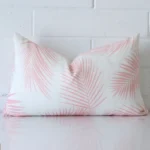 Pink cushion cover in front of a white wall. It has a rectangle size and is made from a outdoor material.
