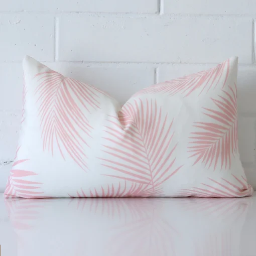 Pink cushion cover in front of a white wall. It has a rectangle size and is made from a outdoor material.