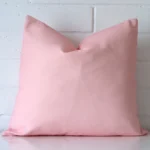 An attractive outdoor cushion in front of a white brick wall. It has a Square shape and is pink in colour.
