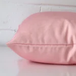 Square outdoor cushion cover positioned flat to show seams. The pink hue is shown between front and rear fabric panels.