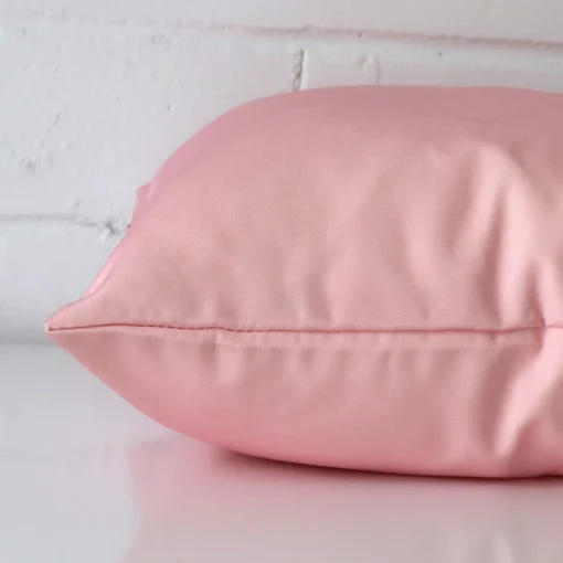 Square outdoor cushion cover positioned flat to show seams. The pink hue is shown between front and rear fabric panels.